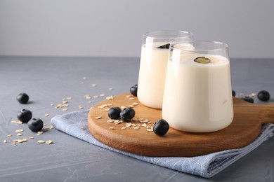 Tasty yogurt in glasses, oats and blueberries on grey table, space for text