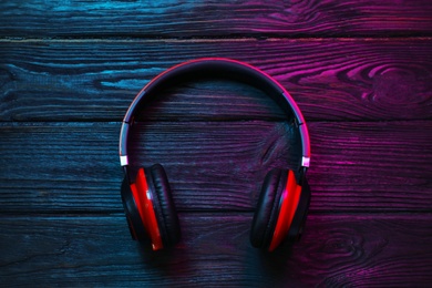 Photo of Stylish modern headphones with earmuffs on wooden background, top view