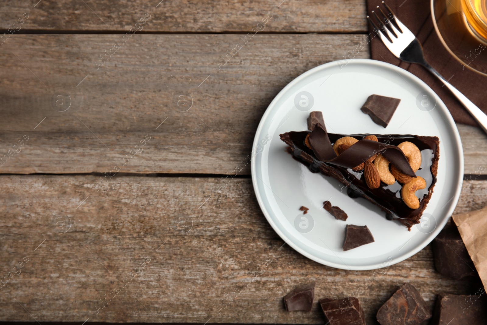 Photo of Piece of tasty homemade chocolate cake with nuts on wooden table, flat lay. Space for text