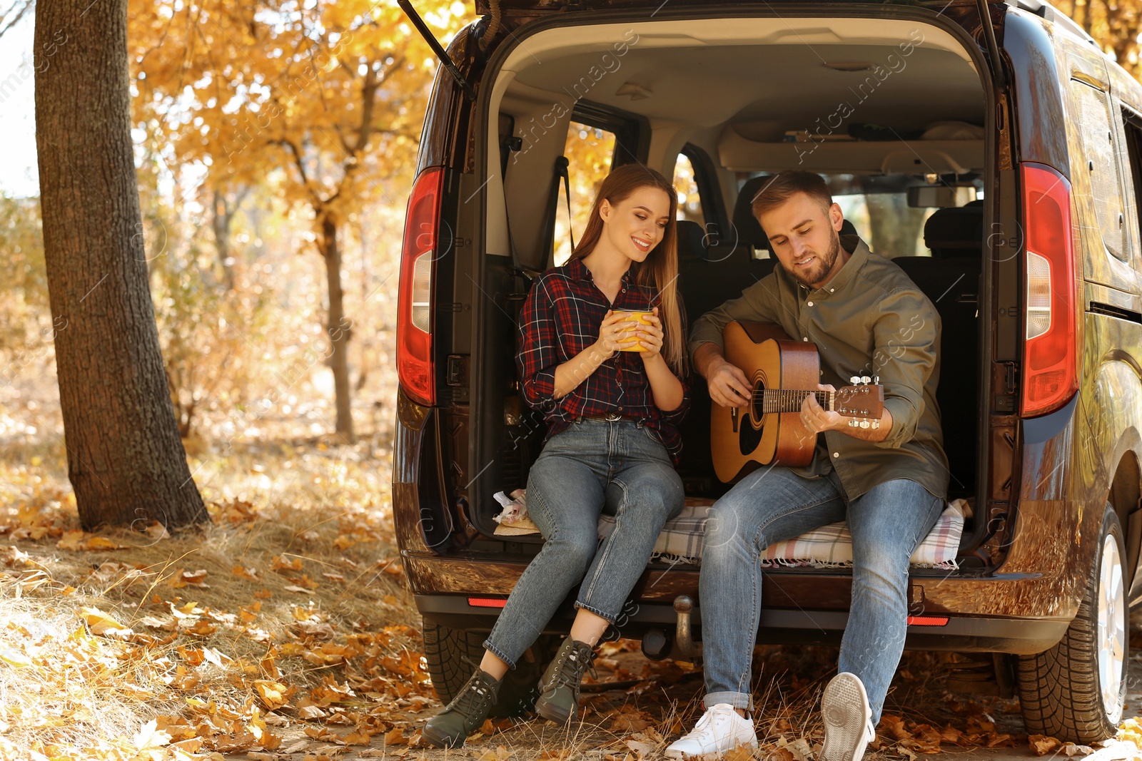 Photo of Young couple with guitar sitting in open car trunk outdoors