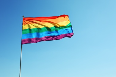 Photo of Rainbow LGBT flag and space for text on blue sky background. Gay rights movement