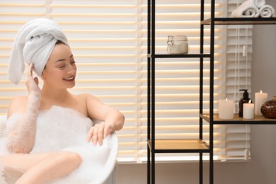 Happy woman taking bath with foam in tub indoors