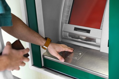 Man entering PIN code on cash machine keypad outdoors, closeup