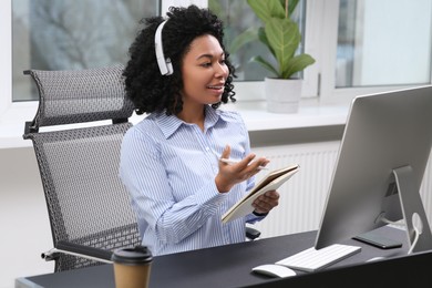 Young woman with headphones having video chat via computer in office