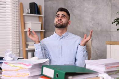 Overwhelmed man surrounded by documents at workplace in office