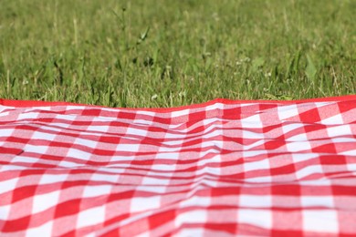 Checkered picnic tablecloth on fresh green grass, closeup