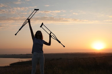 Woman holding axillary crutches outdoors at sunrise. Healing miracle
