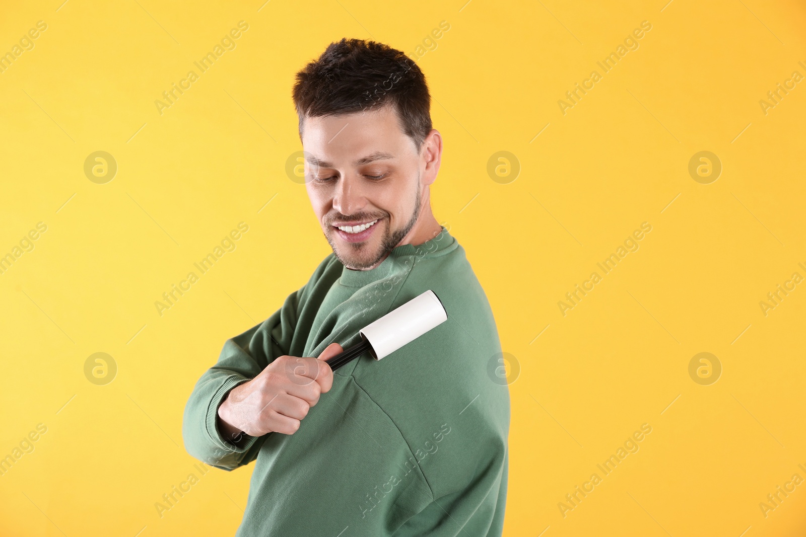 Photo of Man cleaning clothes with lint roller on yellow background