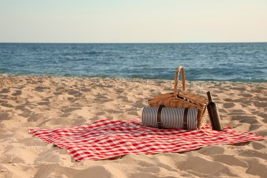 Photo of Blanket with picnic basket and bottle of wine on sandy beach near sea, space for text