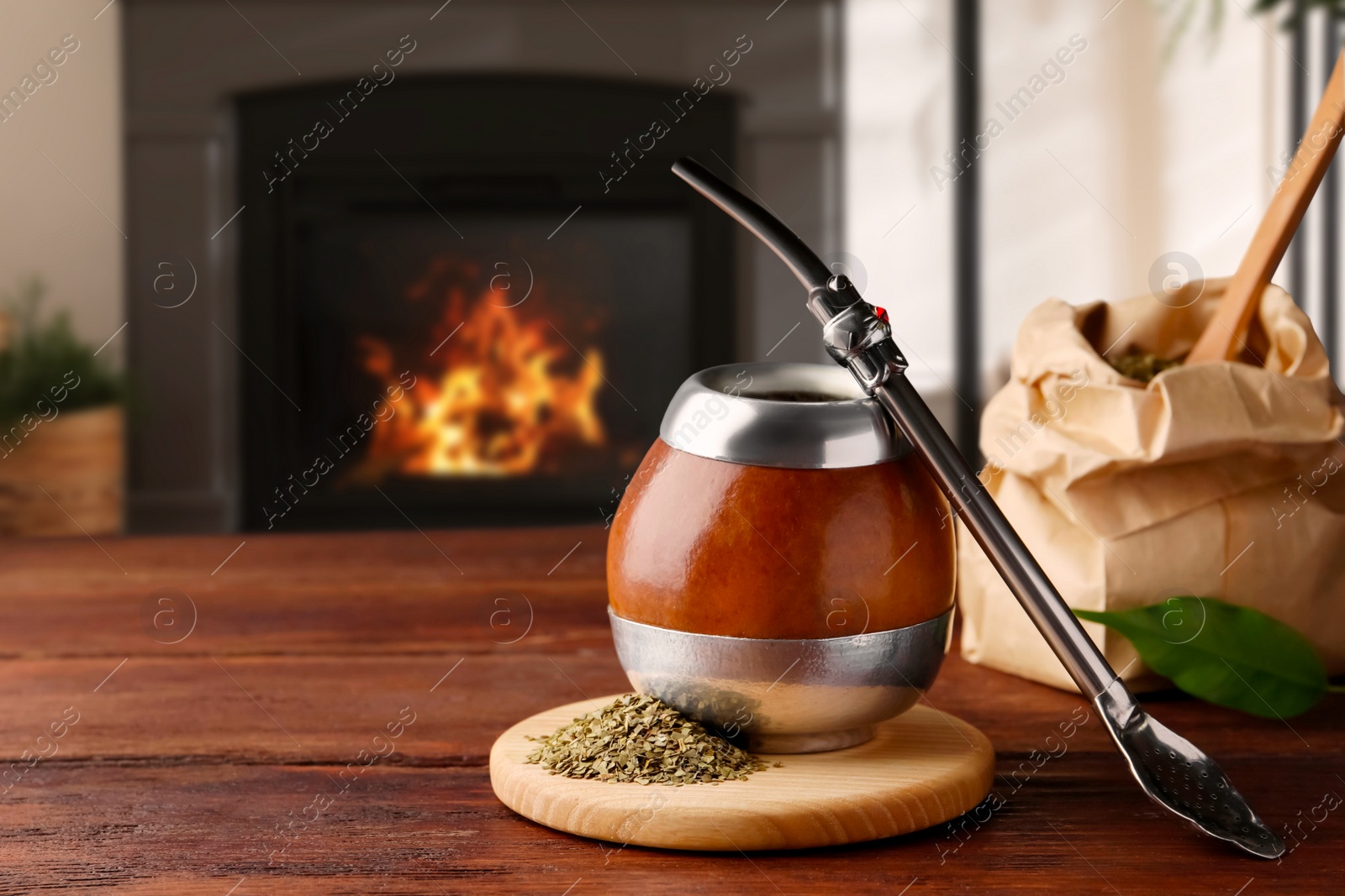 Image of Calabash with mate tea and bombilla on wooden table near fireplace. Space for text