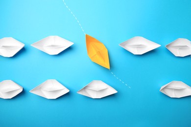 Photo of Yellow paper boat floating through others on light blue background, flat lay. Uniqueness concept