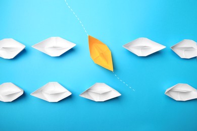 Yellow paper boat floating through others on light blue background, flat lay. Uniqueness concept