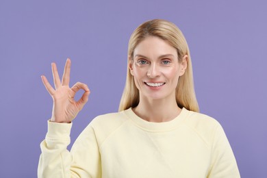 Photo of Woman with clean teeth smiling and showing OK gesture on violet background
