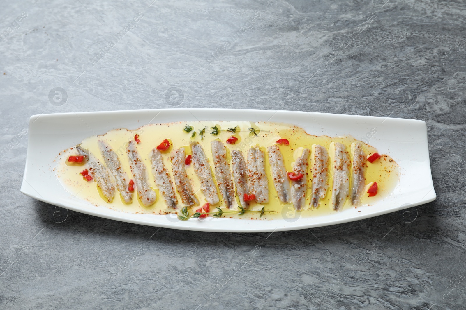 Photo of Tasty pickled anchovies with spices on gray table, above view