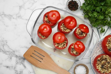 Photo of Delicious stuffed tomatoes with minced beef, bulgur and mushrooms in glass baking dish on white marble table, flat lay