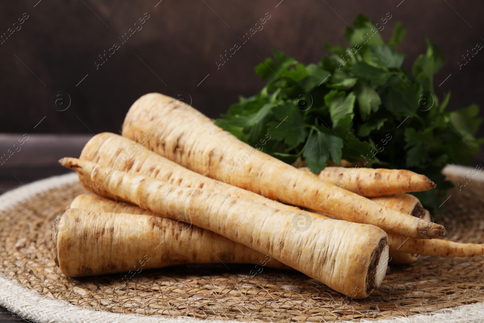 Photo of Raw parsley roots and fresh herb on wicker mat, closeup