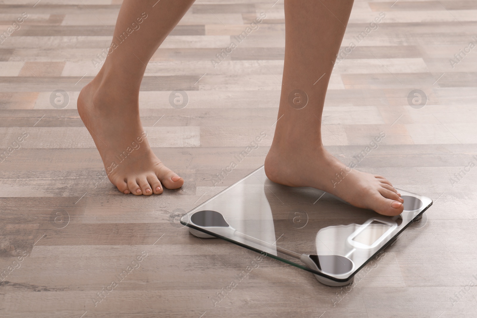 Photo of Woman stepping on floor scales indoors, closeup. Weight control