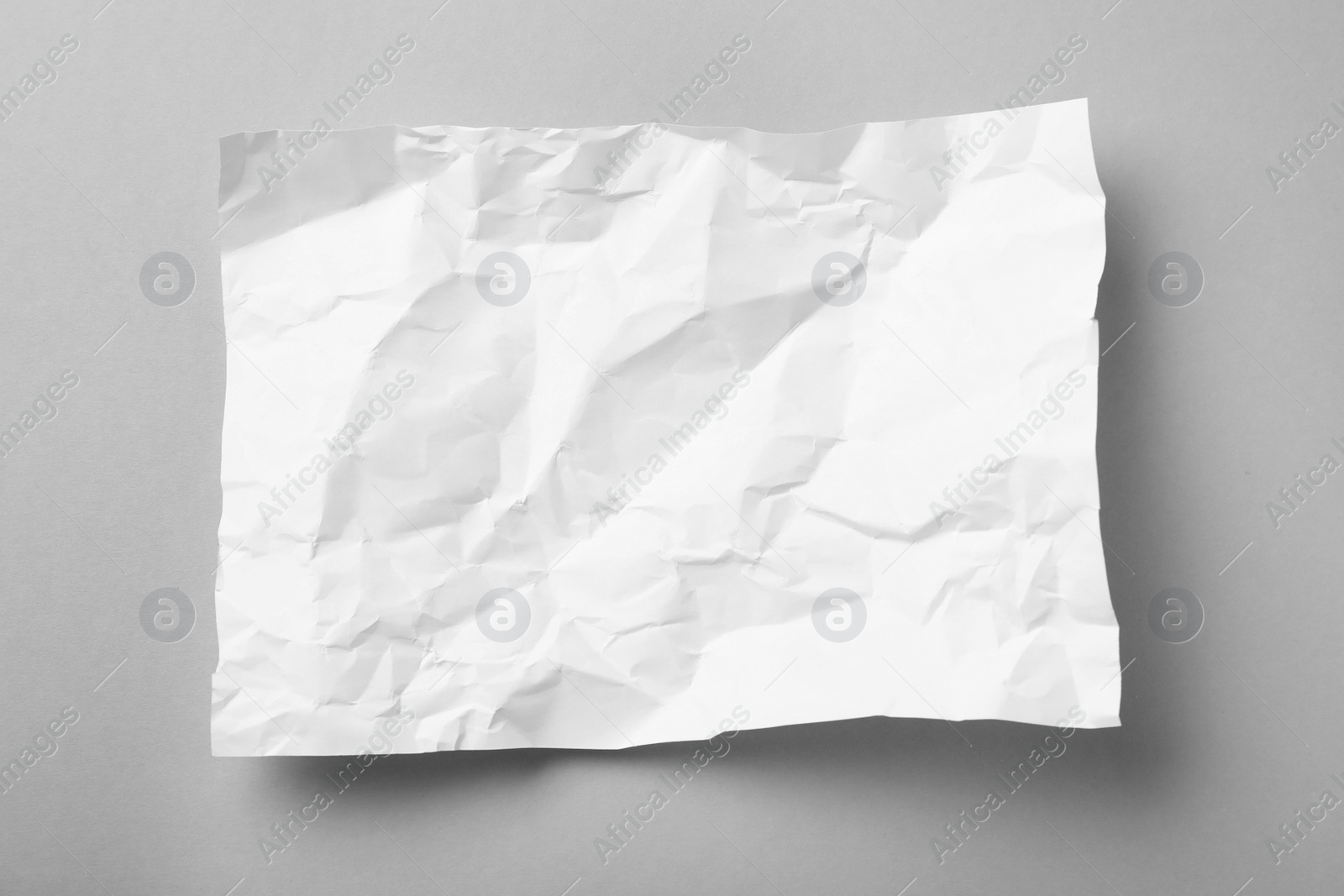 Photo of Sheet of white crumpled paper on grey background, top view