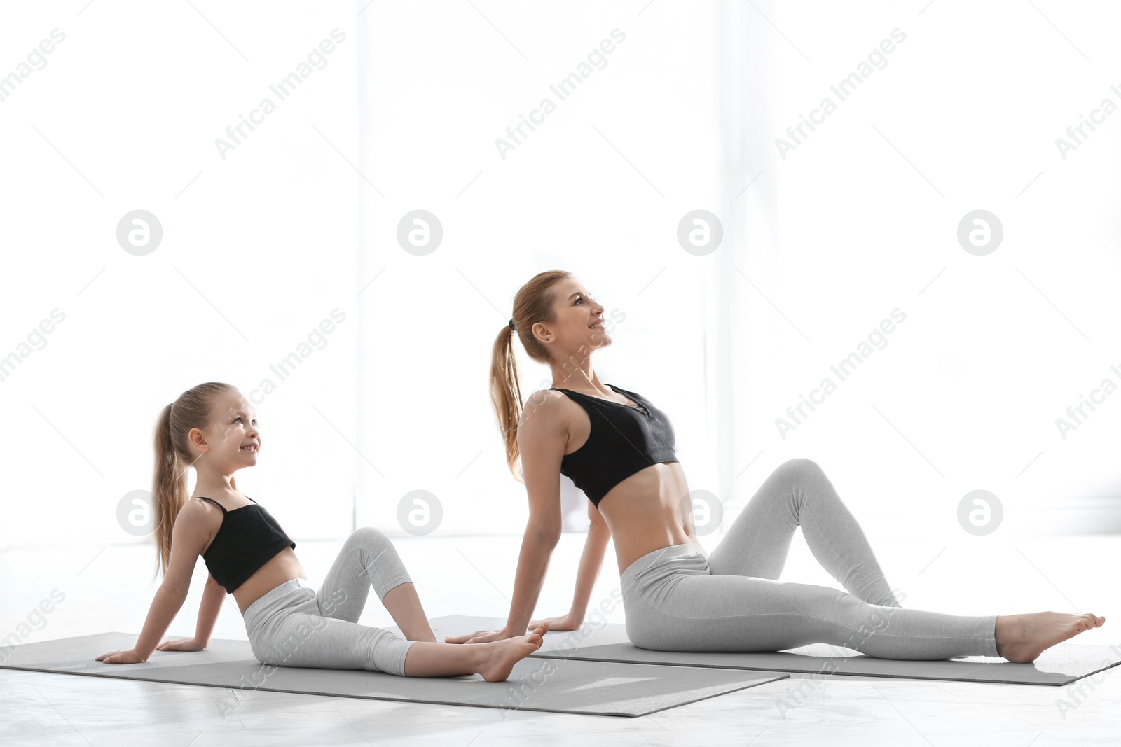 Photo of Mother and daughter in matching sportswear doing yoga together at home