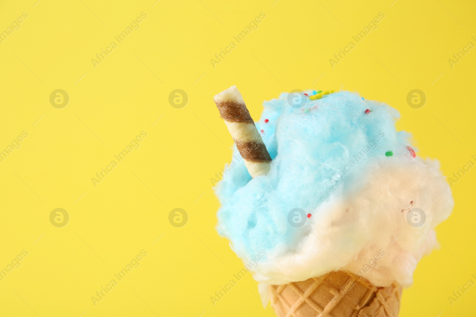 Photo of Sweet cotton candy in waffle cone on yellow background, closeup. Space for text