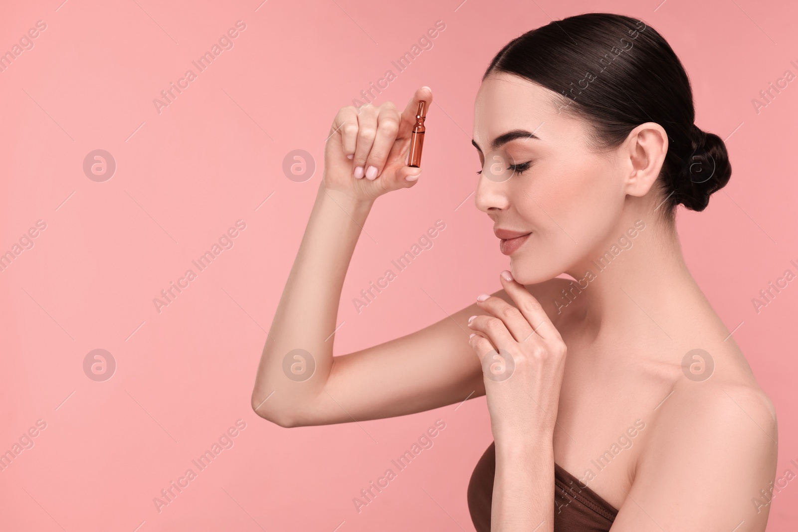 Photo of Beautiful young woman holding skincare ampoule on pink background. Space for text