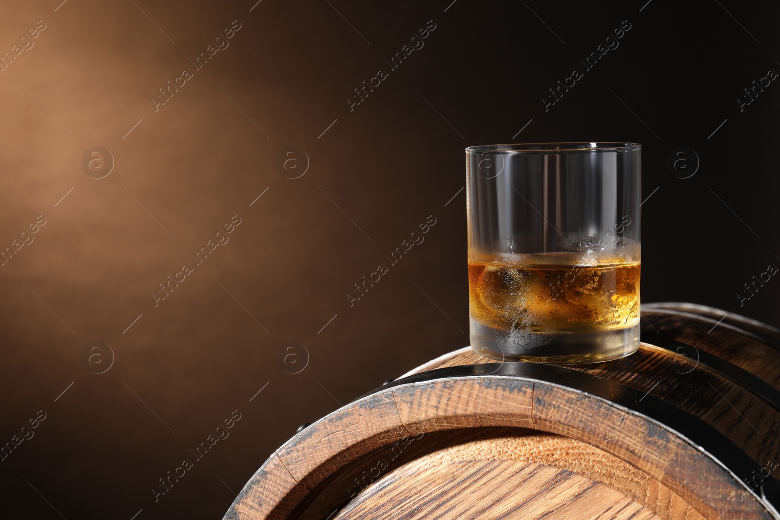 Photo of Glass of tasty whiskey on wooden barrel against dark background, space for text