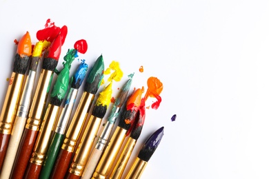 Photo of Brushes with colorful paints on white background, flat lay. Space for text