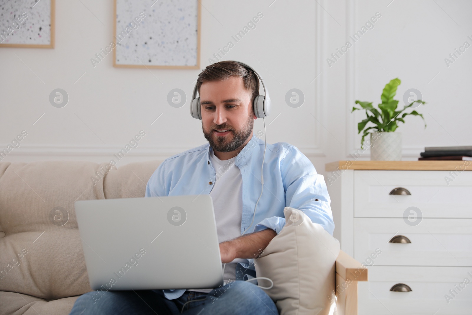 Photo of Man with laptop and headphones sitting on sofa at home