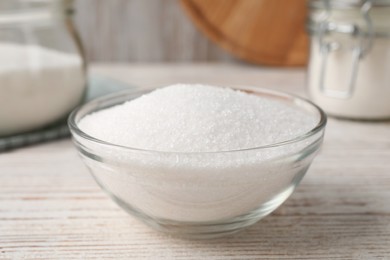 Photo of Granulated sugar in glass bowl on white wooden table, closeup