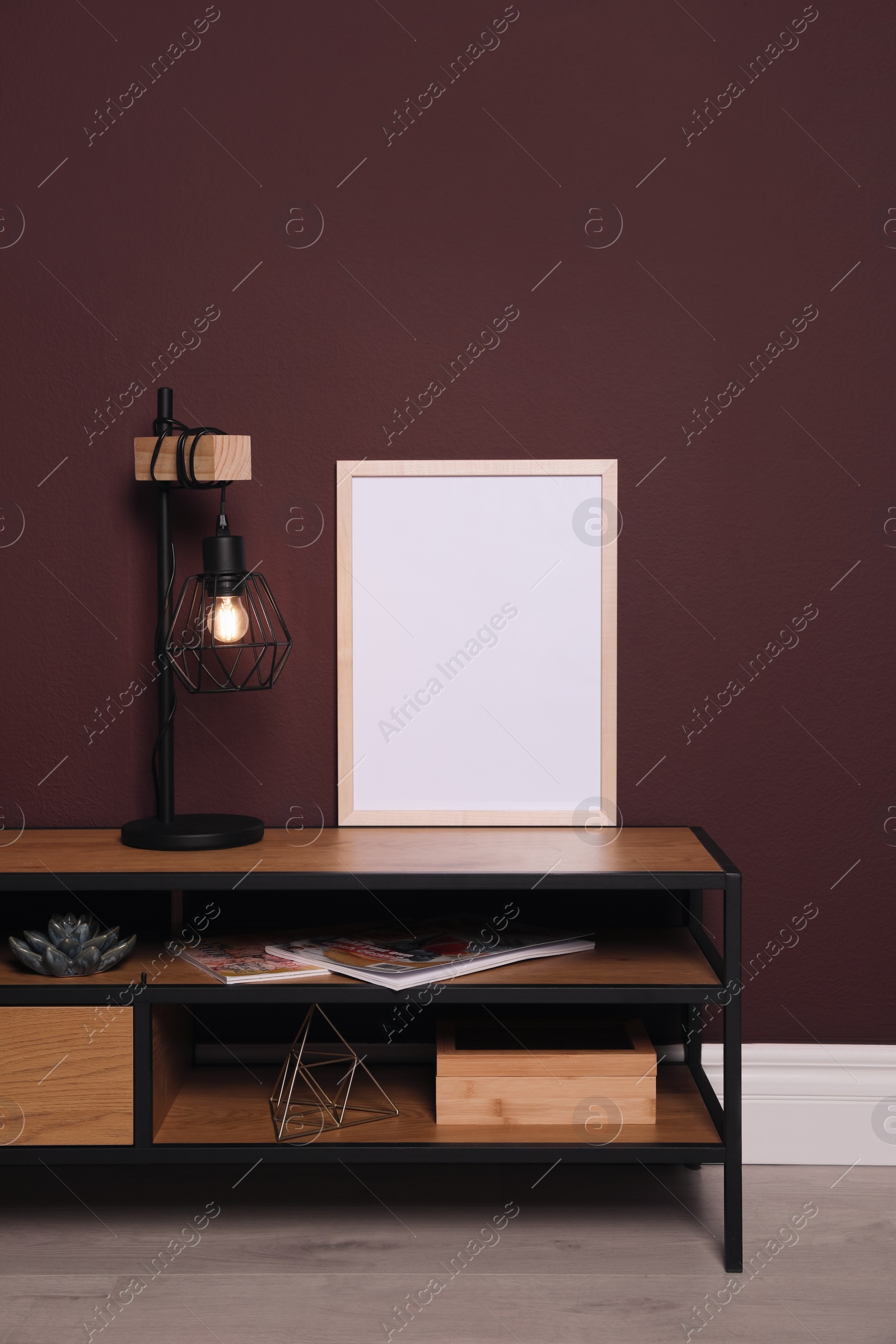 Photo of Empty frame and stylish lamp on wooden table near brown wall. Mockup for design