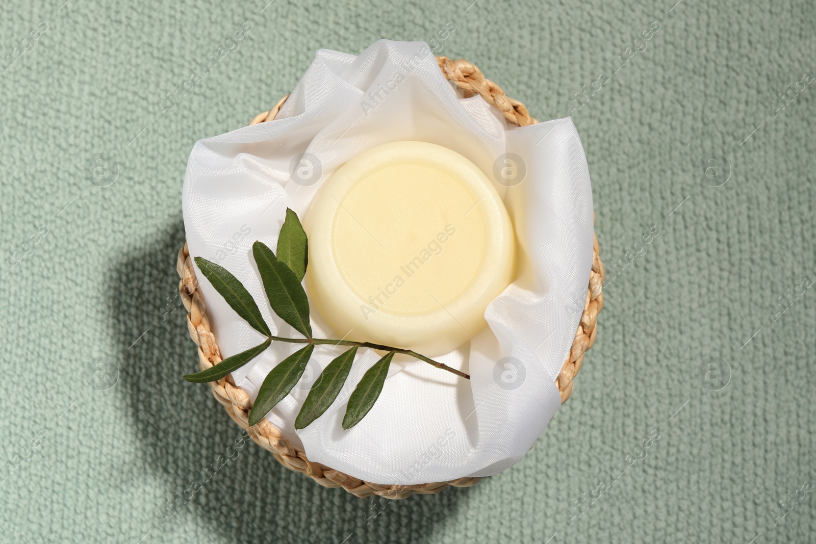 Photo of Solid shampoo bar in wicker basket on pale green fabric, top view