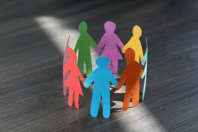 Photo of Paper human figures making circle on wooden table. Diversity and inclusion concept