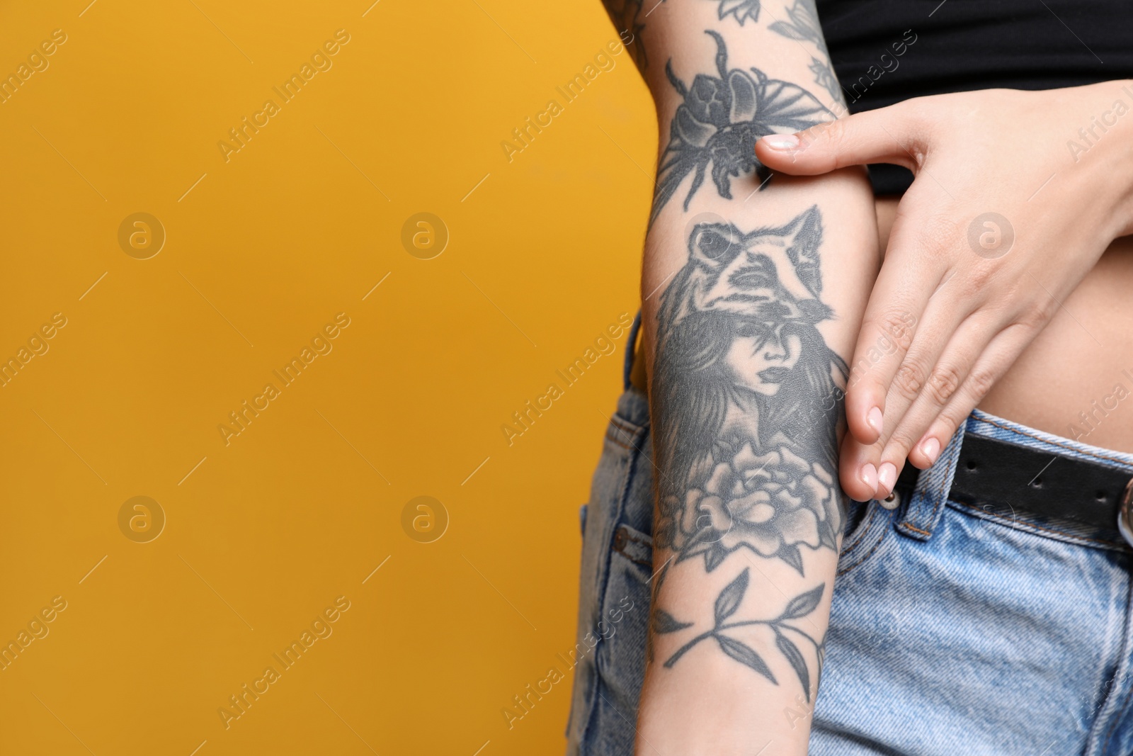 Photo of Woman with tattoos on arm against yellow background, closeup. Space for text