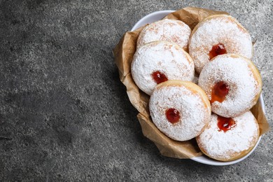 Photo of Delicious donuts with jelly and powdered sugar in bowl on grey table, top view. Space for text