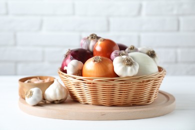 Photo of Fresh raw garlic and onions in wicker basket on white table