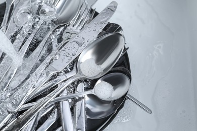 Photo of Washing silver spoons, forks and knives under stream of water in kitchen sink, flat lay. Space for text