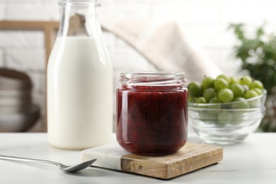 Jar of delicious gooseberry jam, fresh berries and milk on white table