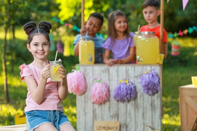 Photo of Cute little girl with natural lemonade in park, space for text. Summer refreshing drink