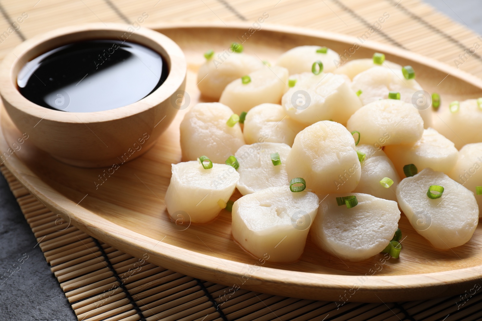 Photo of Raw scallops with green onion and soy sauce on dark table, closeup