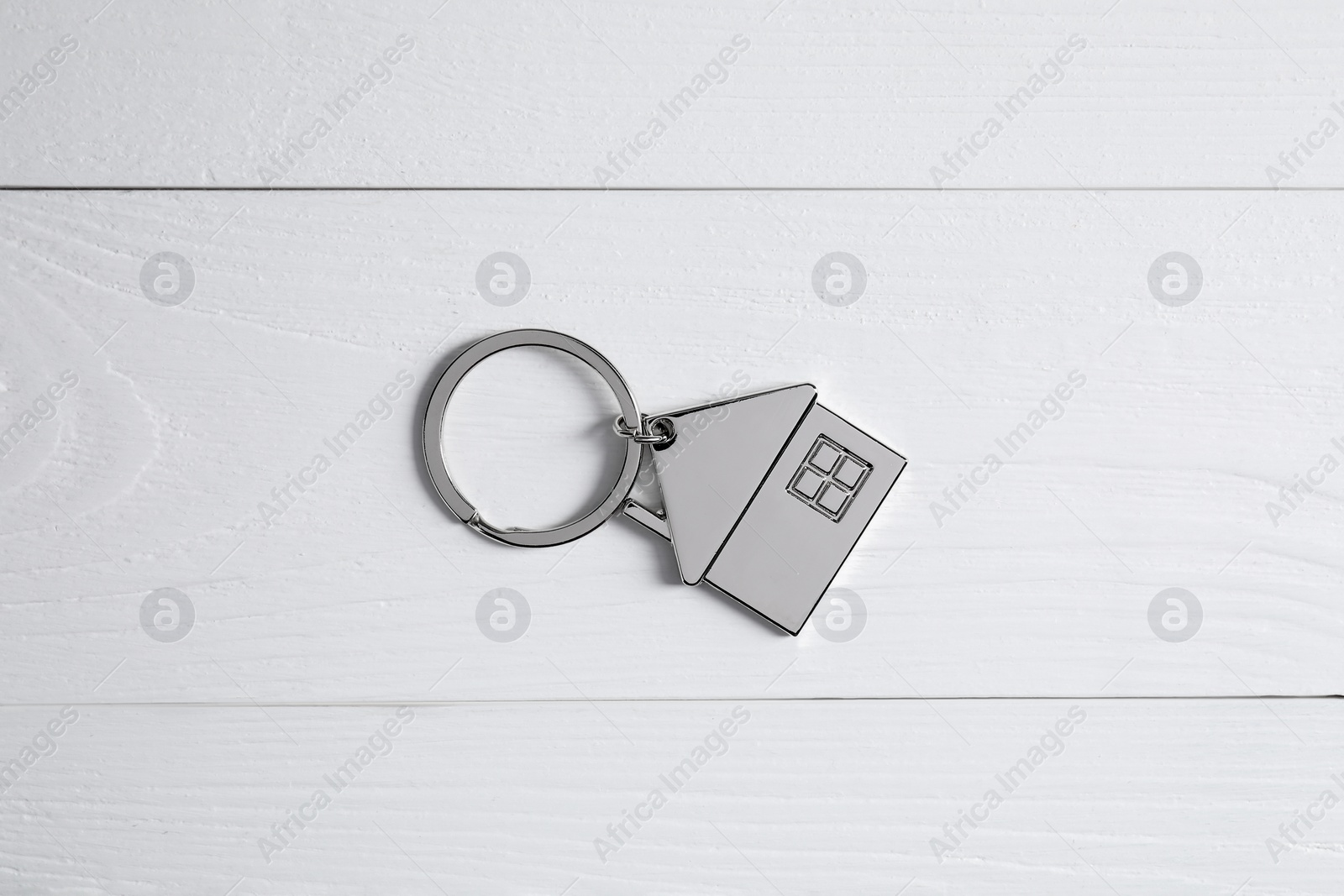 Photo of Metal keychain in shape of house on white wooden table, top view