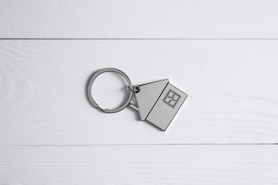 Metal keychain in shape of house on white wooden table, top view