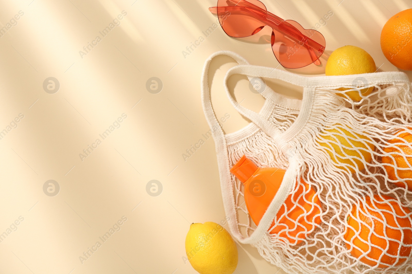 Photo of String bag with fresh fruits, sunscreen and sunglasses on beige background, flat lay. Space for text