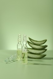 Skincare ampoules with extract of aloe vera and cut leaves on pale green background