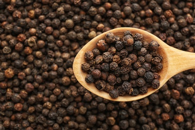 Photo of Spoon with black pepper over heap of grains, top view