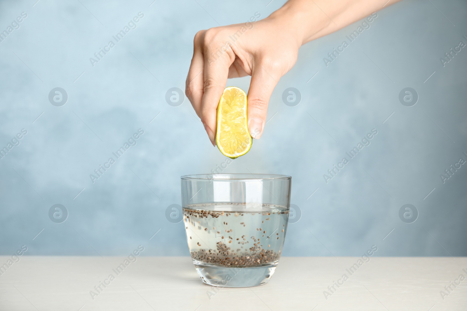 Photo of Young woman squeezing lime into glass of water with chia seeds on table, closeup