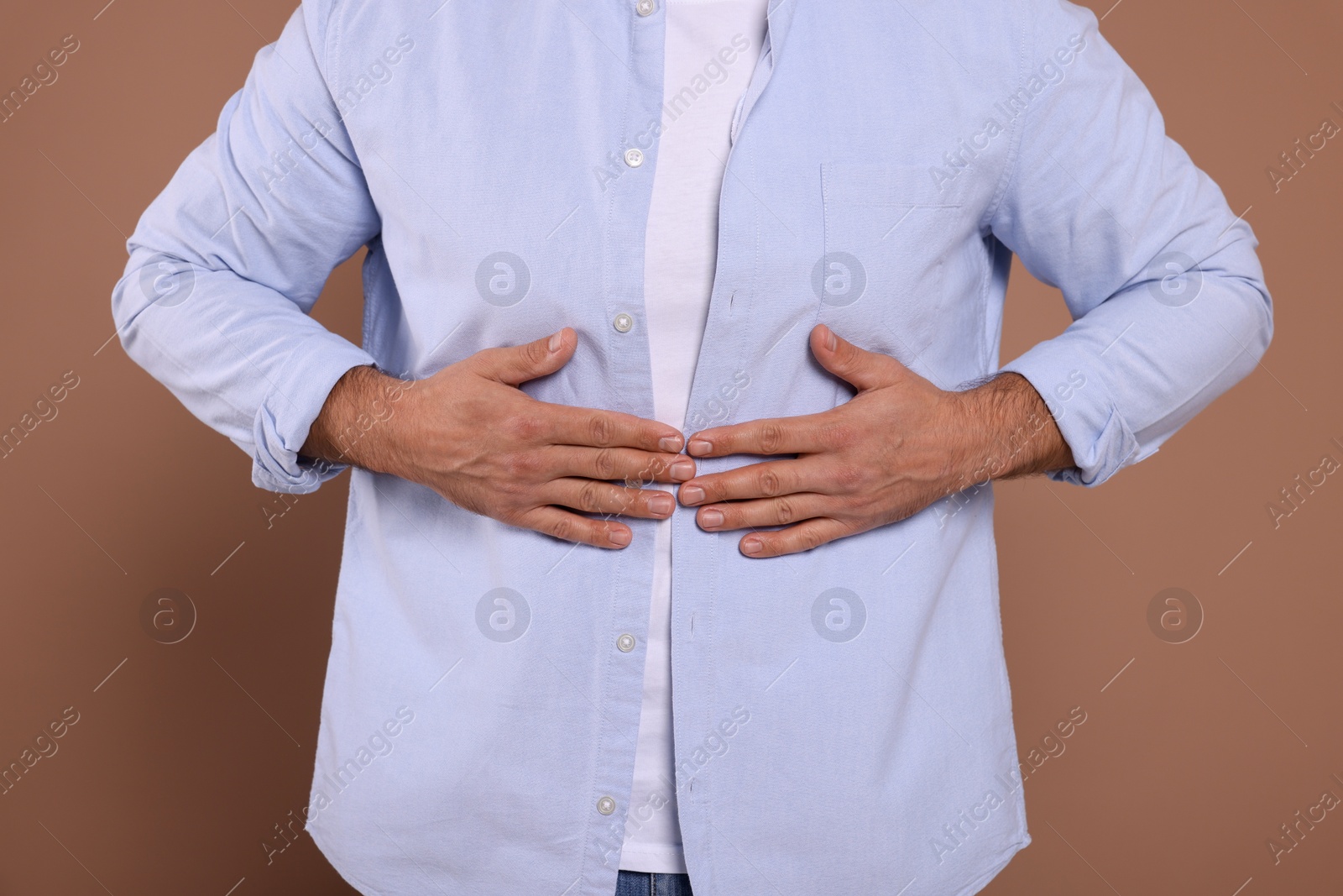 Photo of Man suffering from stomach pain on light brown background, closeup