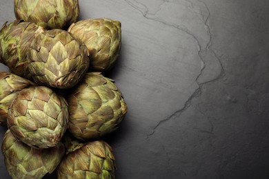 Photo of Fresh raw artichokes on black table, flat lay. Space for text