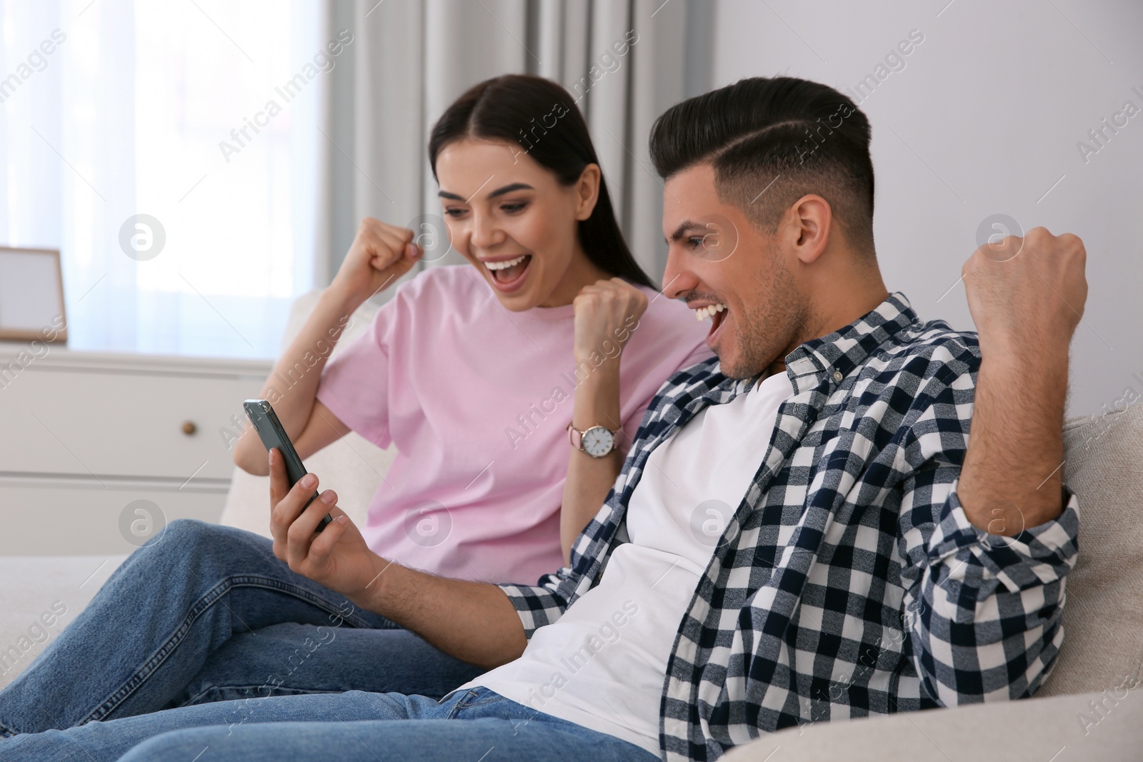 Photo of Emotional couple participating in online auction using smartphone at home