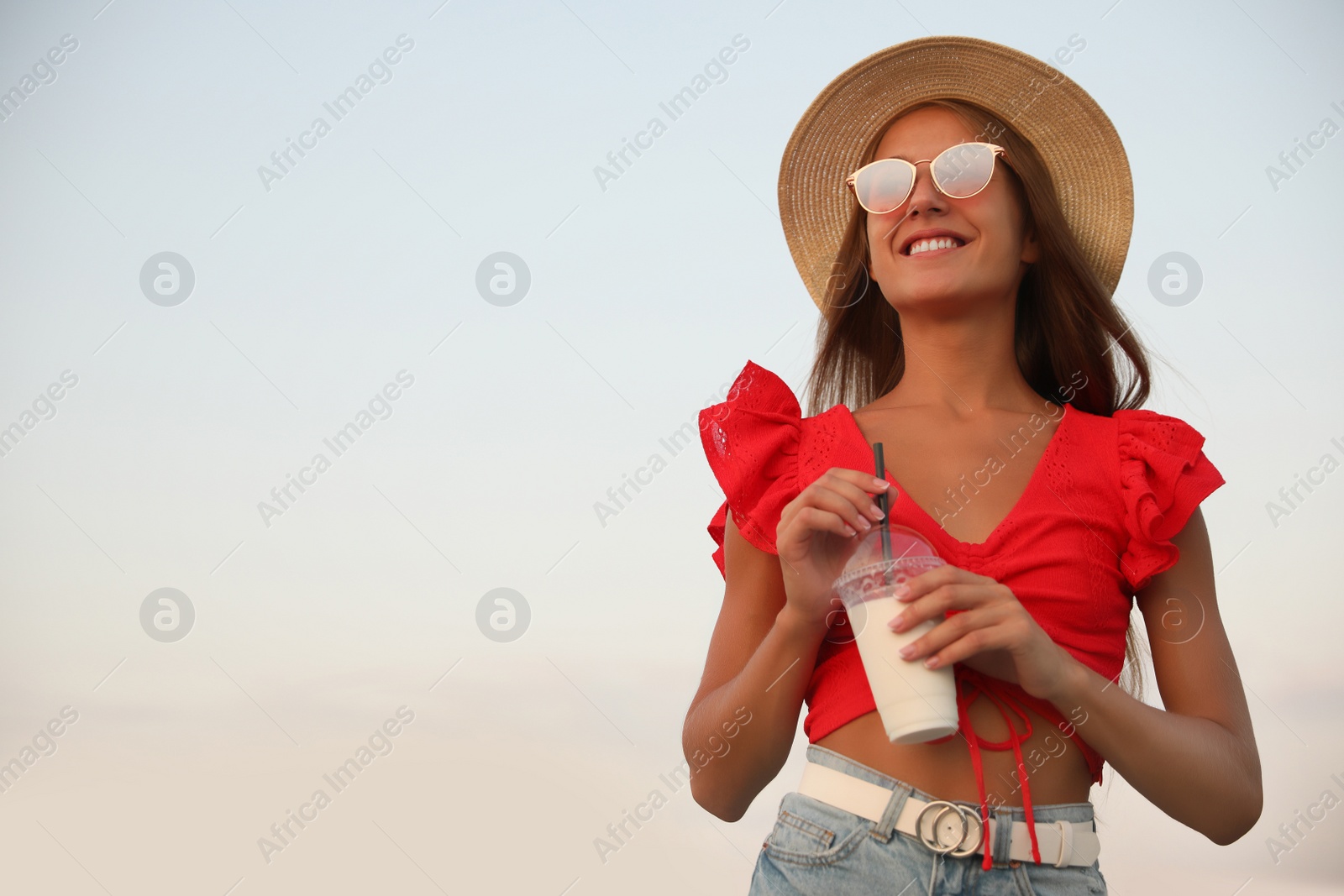 Photo of Beautiful young woman with tasty milk shake outdoors, space for text