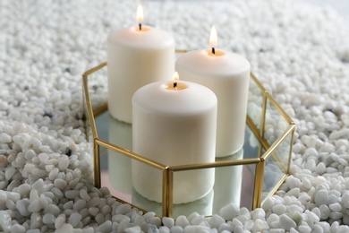 Tray with three white burning candles on rocks